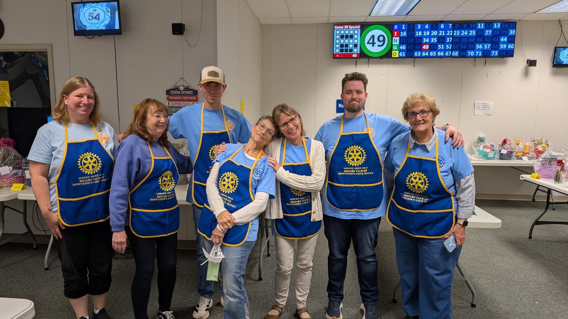 Rotary volunteers in club aprons in front of the bingo number board, Sept. 20, 2026